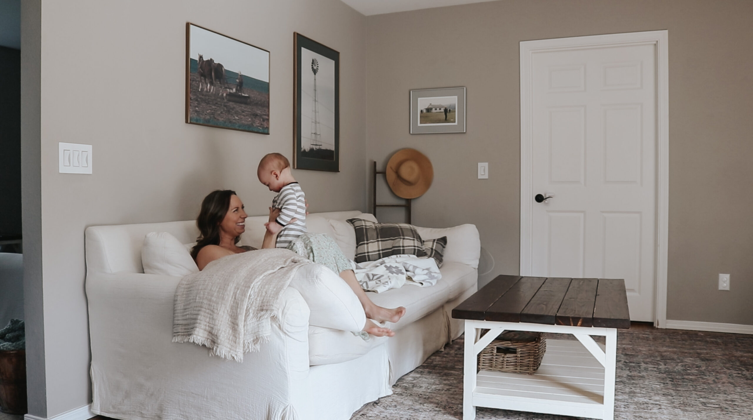Christian homemaker plays with her child on a white couch in living room. There is a coffee table in front of the couch.